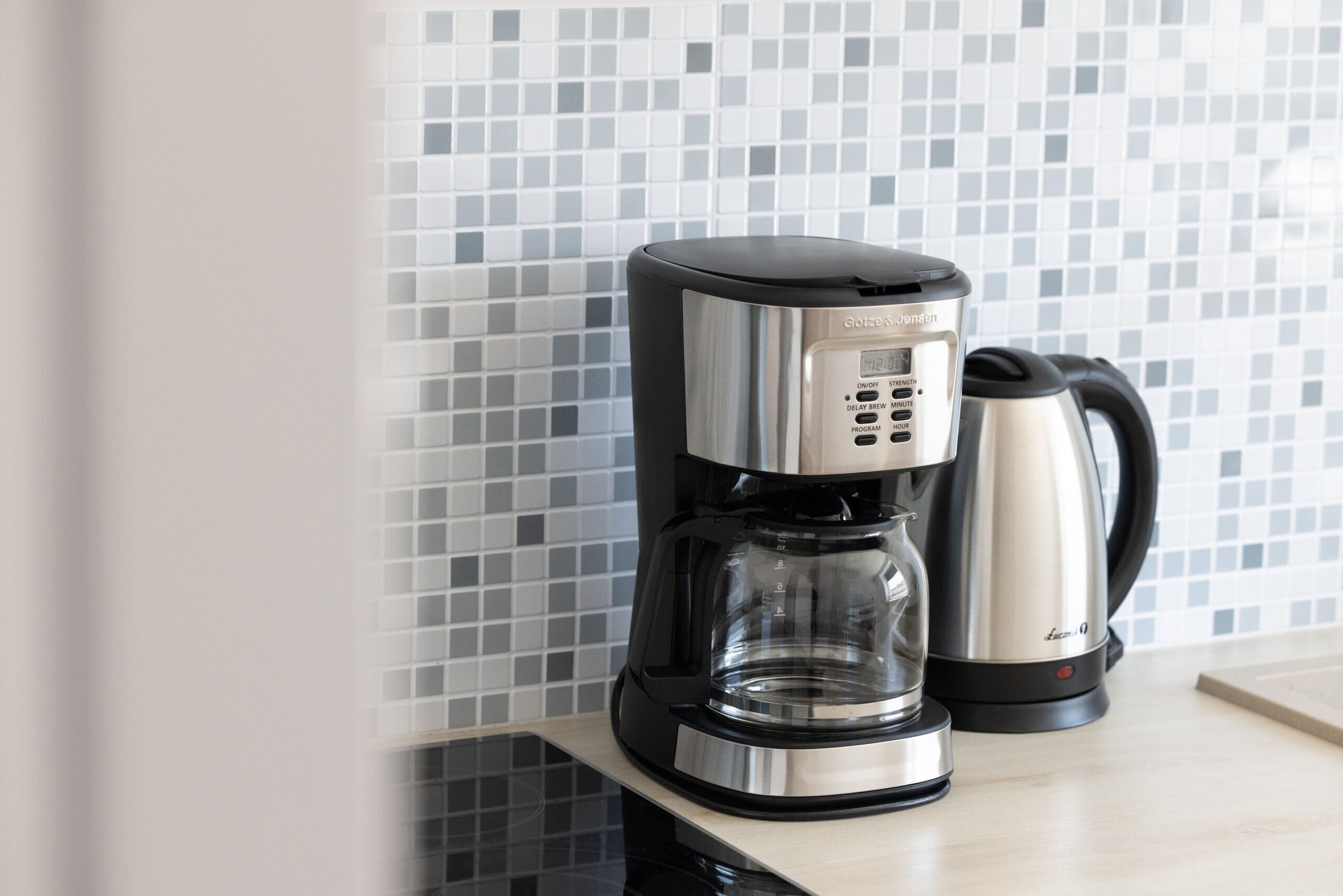 A coffee maker and a kettle on a countertop with a tiled backsplash.