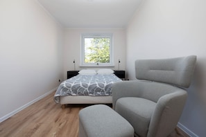 A bedroom with a bed, a window, a chair, and a nightstand.