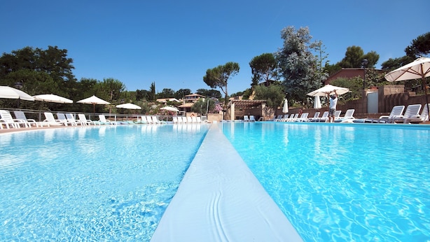 A clear swimming pool with lounge chairs and umbrellas, surrounded by trees and buildings. - Residence con piscina a Guardistallo  (Guardistallo)