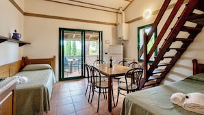 A room with two beds, a wooden table with chairs, a staircase, and a door leading to an outdoor area. - Residence con piscina a Guardistallo  (Guardistallo)