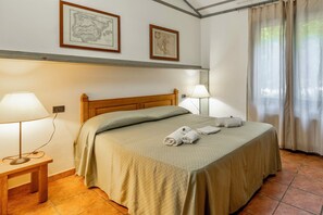 A neatly made bed with a green bedspread and two rolled towels, a wooden nightstand with a lamp, and two framed maps on the wall. - Residence con piscina a Guardistallo  (Guardistallo)