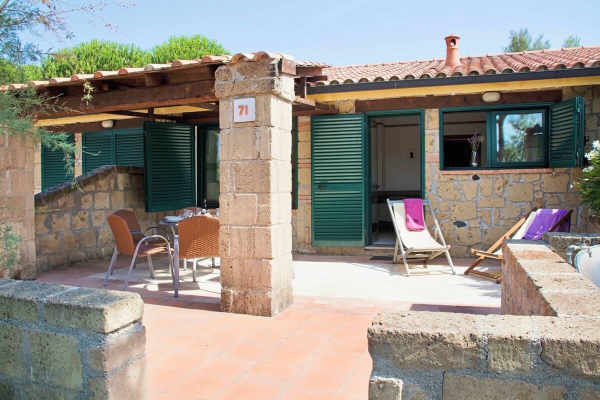 A stone building with a tiled roof, numbered 71, featuring outdoor seating with chairs and tables, and a small patio area.
