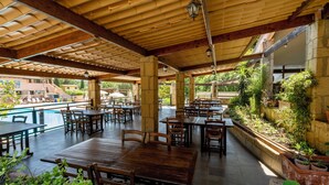 An outdoor patio area with wooden tables and chairs, a pool, and a stone wall with plants. - Residence con piscina a Guardistallo  (Guardistallo)