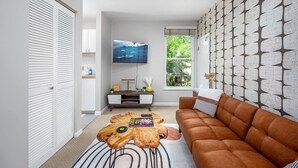 A living room with a brown sofa, a wooden coffee table, a flat-screen TV, and a patterned wall. - Charming Loft 5 Min Walk to Duke University (Durham)