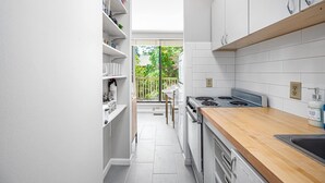 A narrow kitchen with white cabinets, a wooden countertop, and a view of a balcony. - Charming Loft 5 Min Walk to Duke University (Durham)