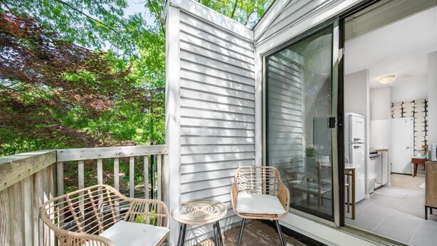A balcony with two wicker chairs and a glass door leading to a kitchen area. - Charming Loft 5 Min Walk to Duke University (Durham)