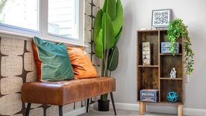 A bench with cushions, a bookshelf with books and a QR code, and a large plant. - Charming Loft 5 Min Walk to Duke University (Durham)