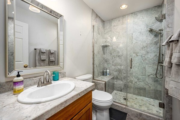A bathroom with a marble sink, a toilet, a glass-enclosed shower, and a mirror with a decorative frame.