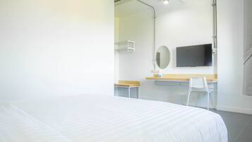Habitación de hotel con cama, escritorio, silla, televisor y espejo.