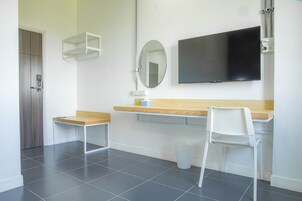 Una habitación moderna con un escritorio de madera, una silla blanca, un espejo y un televisor de pantalla plana montado en la pared.