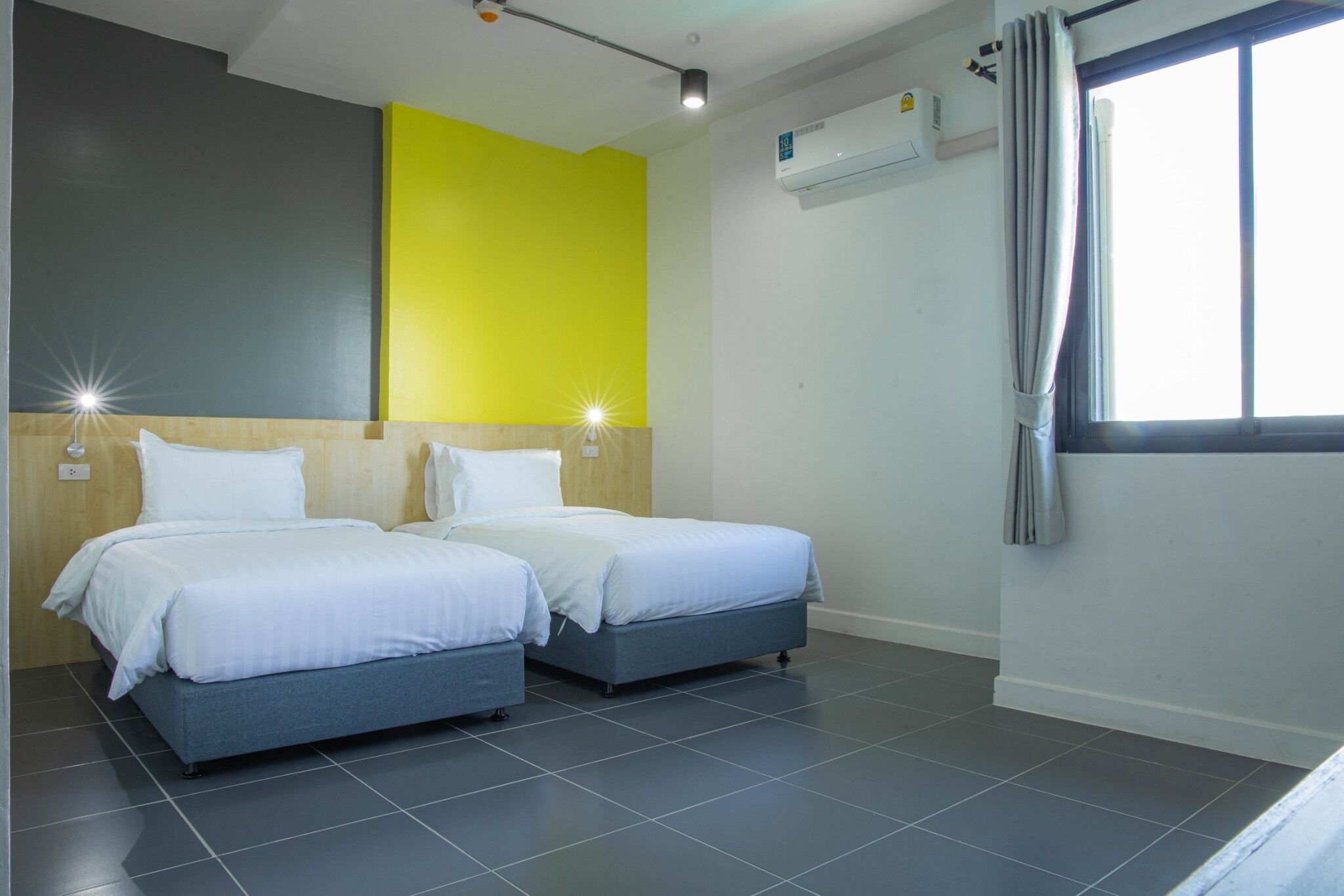 Une chambre d’hôtel avec deux lits, un mur d’accent d’un jaune vif et un appareil de climatisation.