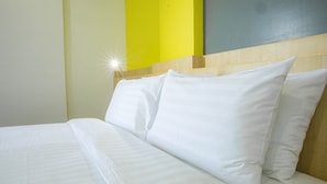 Ein ordentlich bezogenes Bett mit weißen Leinen und Kissen, ein Holzkopfschild und eine leuchtend gelbe Wand.