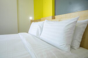 Una cama bien tendida con sábanas y almohadas blancas, un cabecero de madera y una pared de acento amarillo brillante.