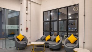 Ein moderner Wartebereich mit grauen Sofas und Sesseln, gelben Kissen und runden Tischen.