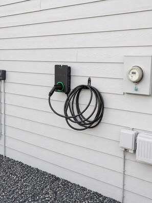 A wall-mounted electric vehicle charging station with a cable and a digital display.