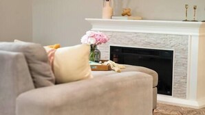 A living room with a beige sofa, a fireplace, a flat-screen TV, and a framed picture on the wall. - HotTub-Fire Pit-Outdoor Dining-EV Charger (East Wenatchee)