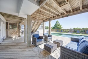 Un espacio al aire libre cubierto con suelo de madera, mobiliario de mimbre y vistas a una piscina.