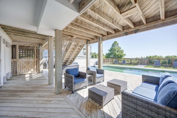 Un espacio al aire libre cubierto con suelo de madera, mobiliario de mimbre y vistas a una piscina.