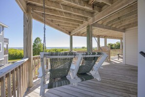 A covered deck with wooden railings, a swing chair, and a view of the ocean.