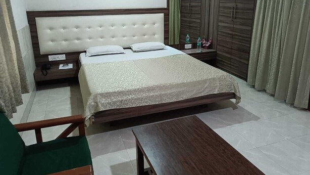 A bedroom with a large bed, wooden wardrobe, and a small table. - Hotel Orchid (Guwahati)