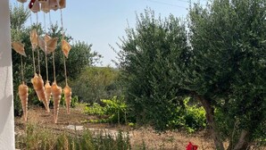 A garden with a pathway, olive trees, and red flowers. - Gorgeous White Marsis Apartment in Paros (Paros)