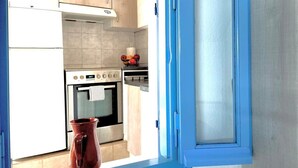 A kitchen with a stove, oven, and cabinets, and a window with a view of the outside. - Gorgeous White Marsis Apartment in Paros (Paros)
