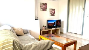 A living room with a sofa, a glass coffee table, a flat-screen TV, and a sliding glass door. - Gorgeous White Marsis Apartment in Paros (Paros)