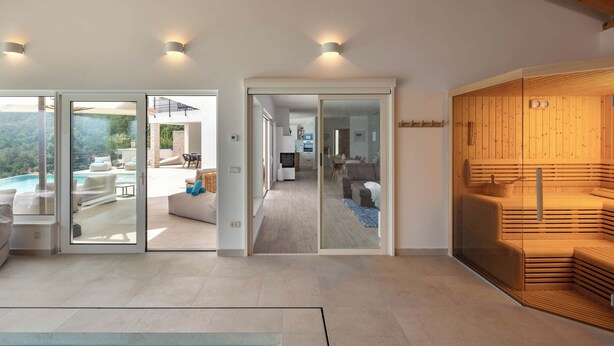 A modern interior with a glass door leading to a pool area, a wooden sauna, and a dining area with a view. - Luxury Villa Dana Indoor Pool and Sauna (Matulji)
