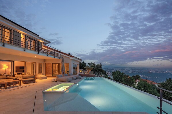 A modern house with a swimming pool, outdoor seating, and a scenic view.