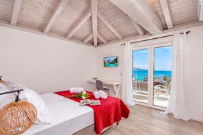 Ein Hotelzimmer mit Bett, Schreibtisch, Stuhl, Fernseher und einem Balkon mit Meerblick.