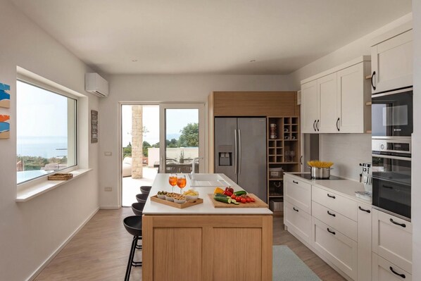 A modern kitchen with a central island, white cabinetry, and a view of the outdoors.