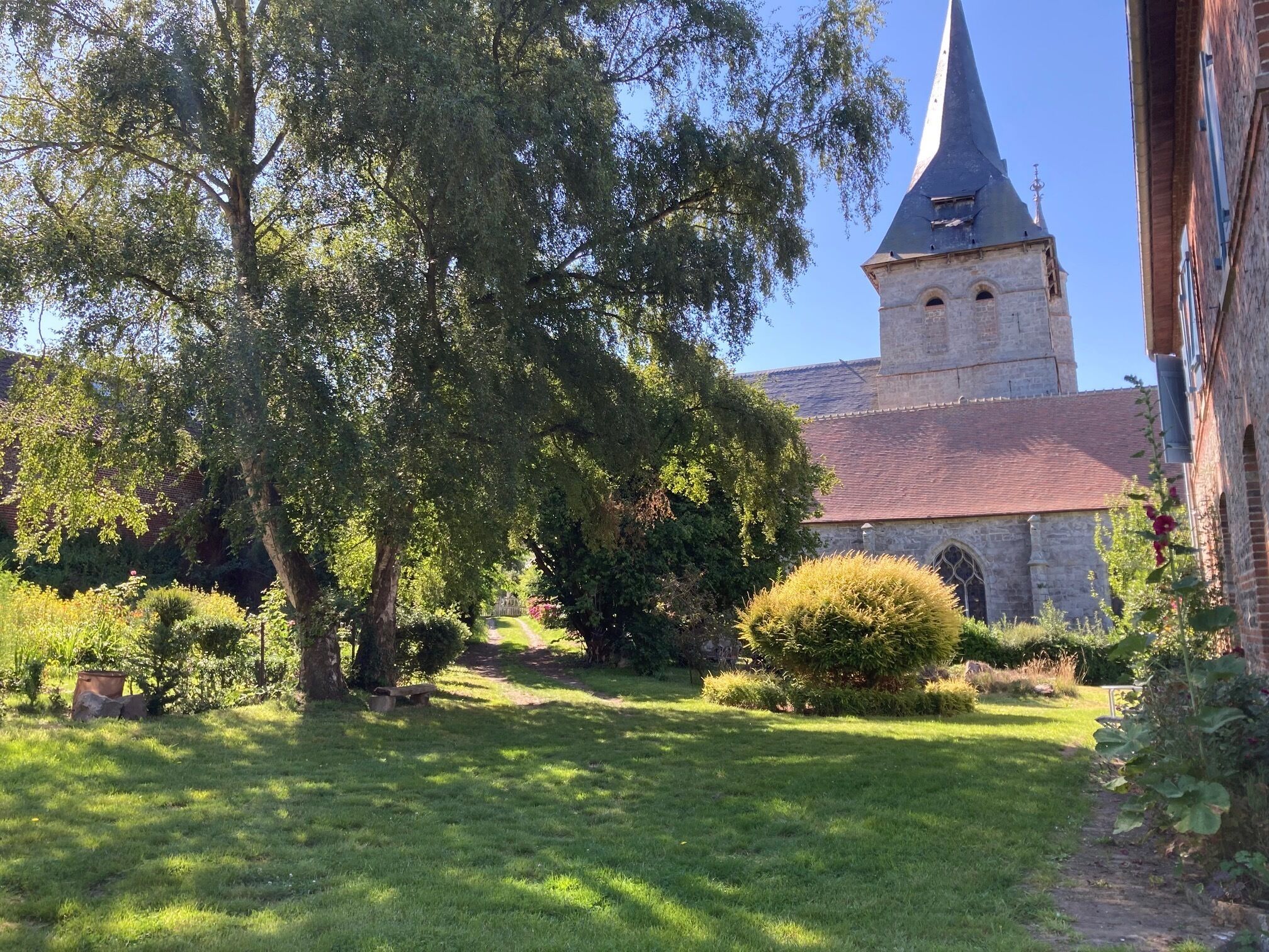 Una chiesa con un campanile slanciato e un giardino con un vialetto che vi conduce.