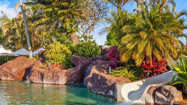 A pool with a water slide, large rocks, and tropical vegetation. - Kolepa Kai: Beautiful 3BR / 3.5BA Home with PBAC Access (Koloa)