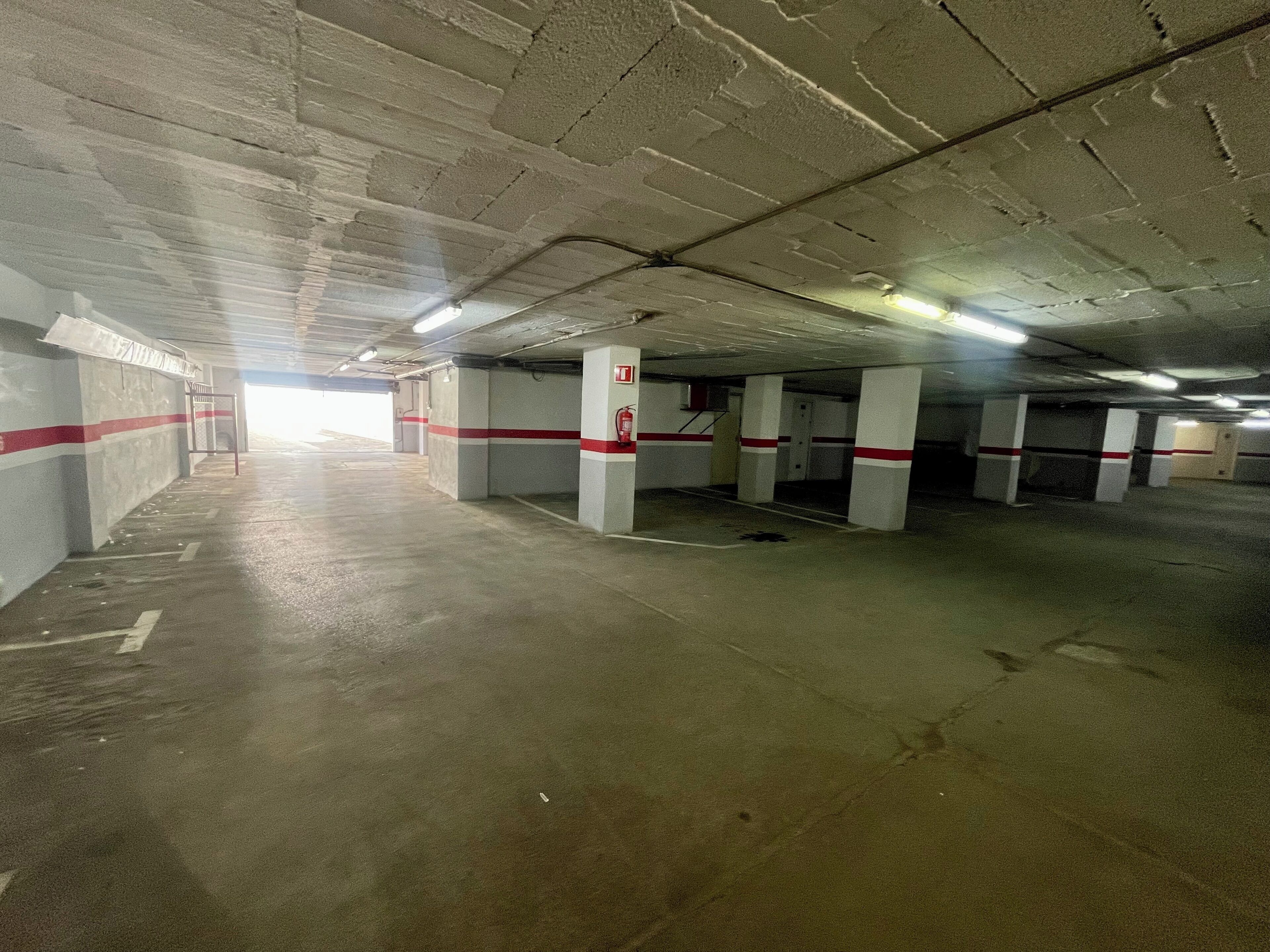 Un estacionamiento subterráneo con pilares de concreto, franjas rojas y blancas, y un extintor.