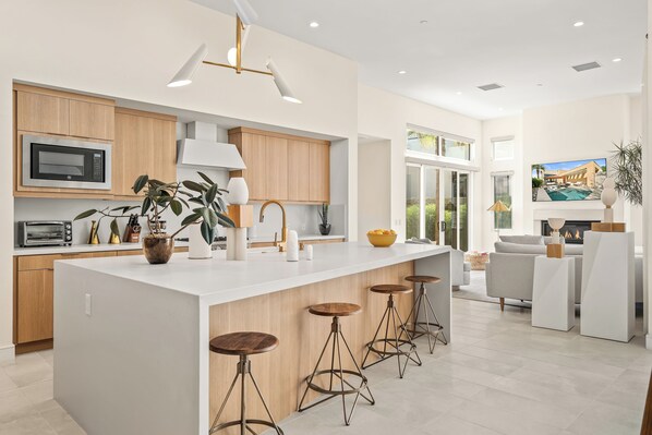 A modern kitchen with a central island, bar stools, and a view of a pool and house.