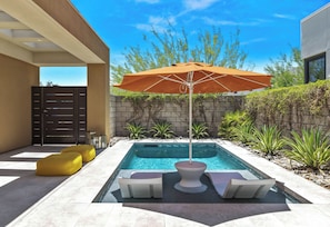 A modern outdoor pool area with a built-in hot tub, a large umbrella, and a seating area with cushions.