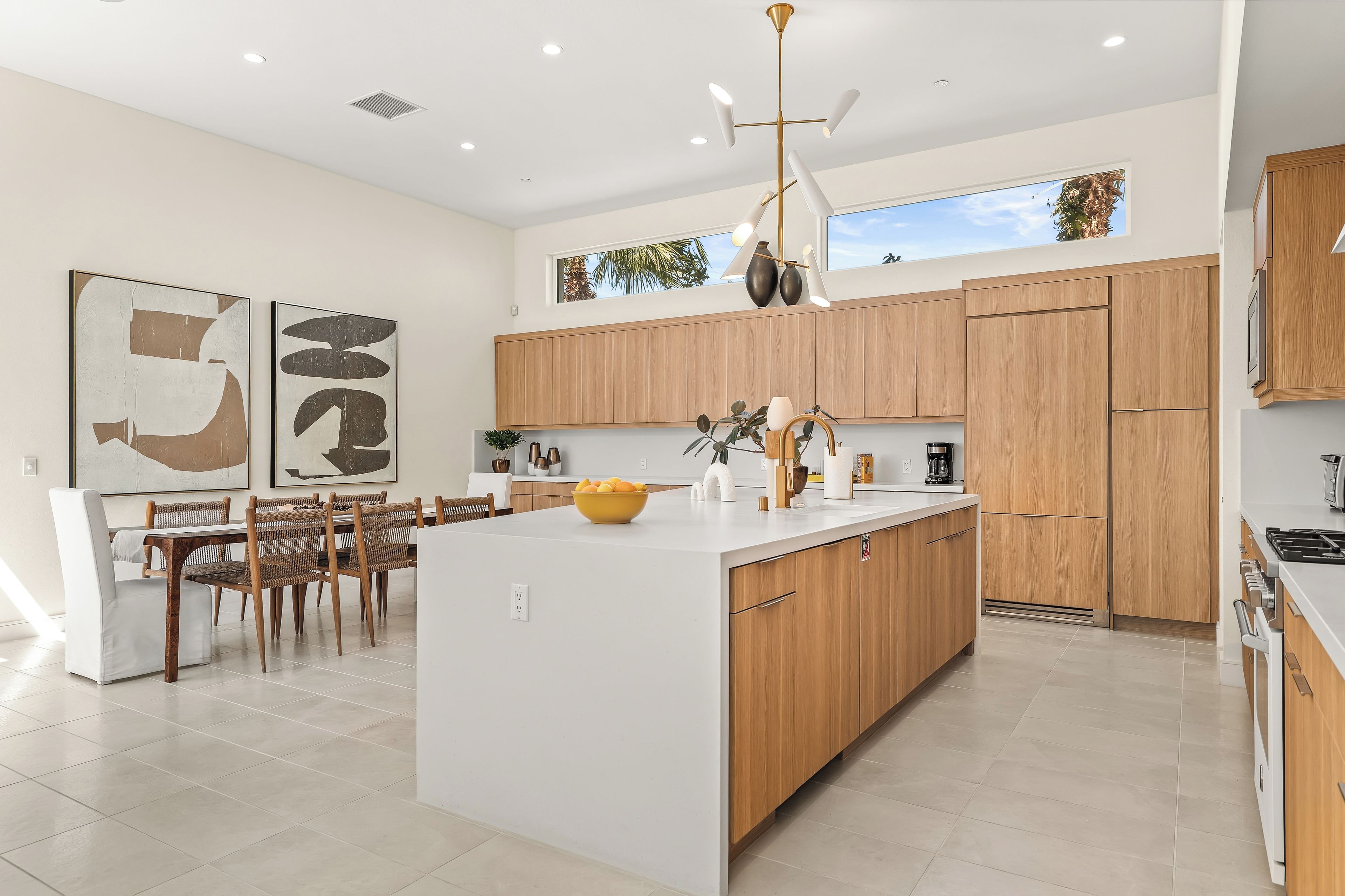 A modern kitchen with wooden cabinets, a central island, and a dining area with chairs.