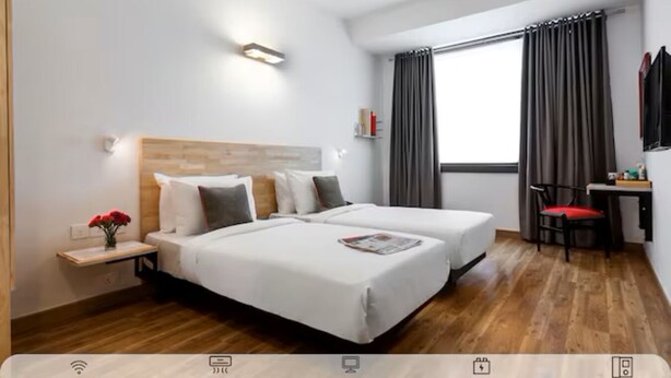 A hotel room with two beds, a desk, a chair, a window with curtains, and a wall-mounted light. - Hotel Golden Key  (New Delhi)