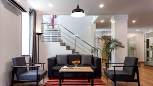 A modern living room with a black sofa, two armchairs, a wooden coffee table, and a red striped rug. A staircase is visible in the background. - Hotel Golden Key  (New Delhi)