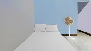 A minimalist hotel room with a single bed, white bedding, and a standing fan. - Hotel O Sukandi Homestay Near The Semeton Homestay (Janapria)