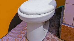 A white toilet in a small bathroom with a tiled floor and a yellow wall. - Hotel O Sukandi Homestay Near The Semeton Homestay (Janapria)