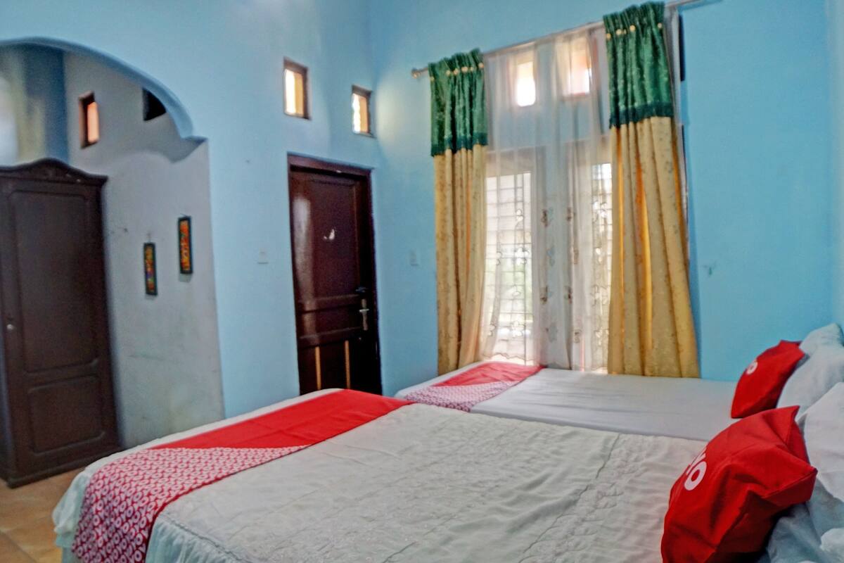 A room with two beds, a wooden wardrobe, a door, and a window with curtains.