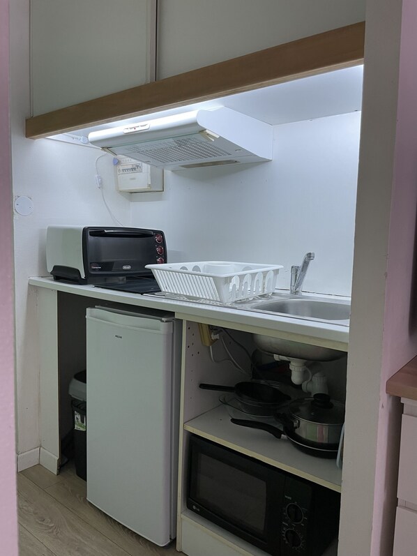 A compact kitchenette with a built-in microwave, a small refrigerator, a toaster, and a sink.