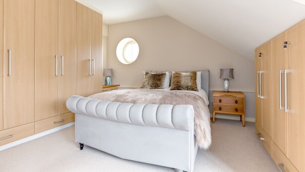 A bedroom with a large bed, wooden wardrobe, and a small bedside table.