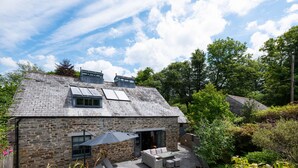 A stone house with a sloped roof, a patio with outdoor furniture, and a garden with various plants.