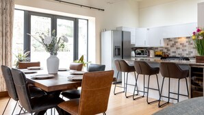 A modern kitchen with a dining area, featuring a large island, bar stools, and a view through the window.