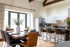 A modern kitchen with a dining area, featuring a large island, bar stools, and a view through the window.