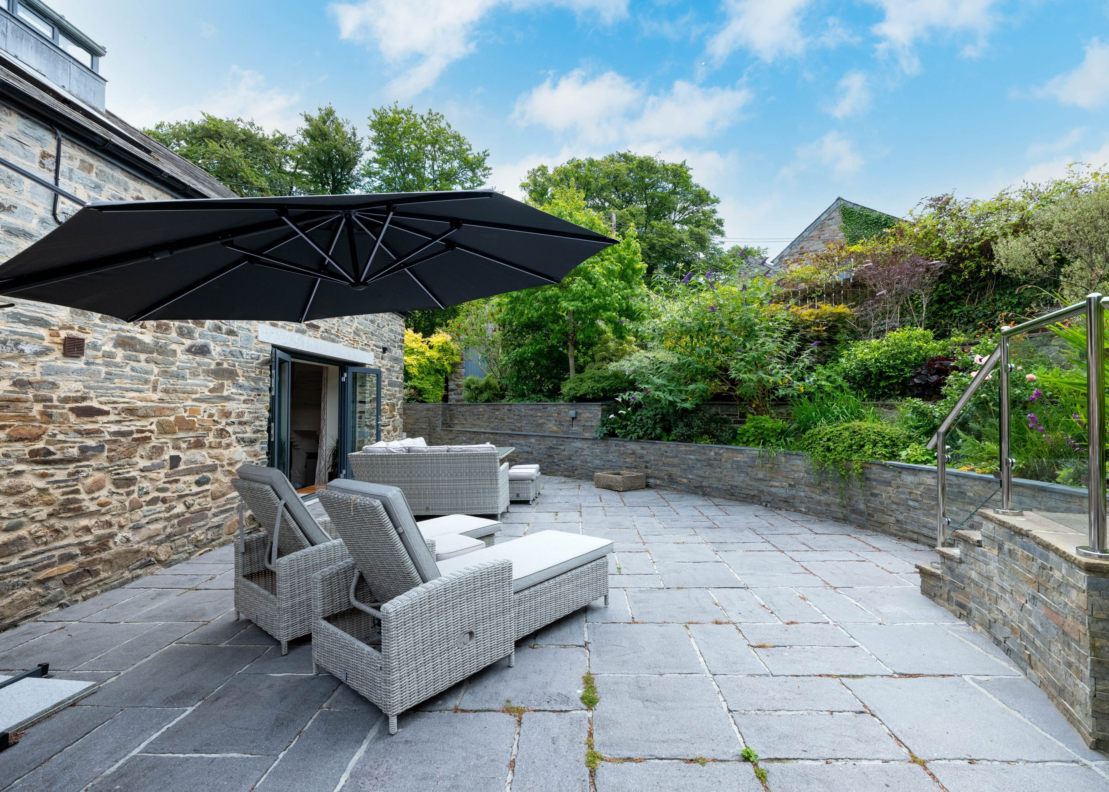 Une terrasse avec un sol en pierre, des meubles en osier et un grand parasol.