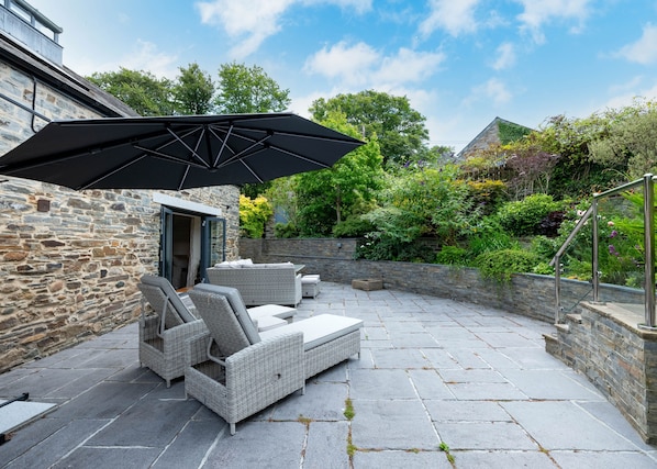A patio with stone flooring, wicker furniture, and a large umbrella.