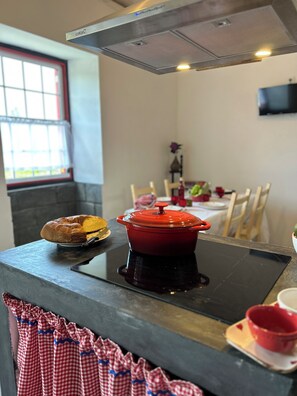 A kitchen with a red pot on an induction cooktop, a loaf of bread, and a window with a view of the outdoors. - Casa Tradicional da Ilha do Pico a 300 Metros da Água (Açores)